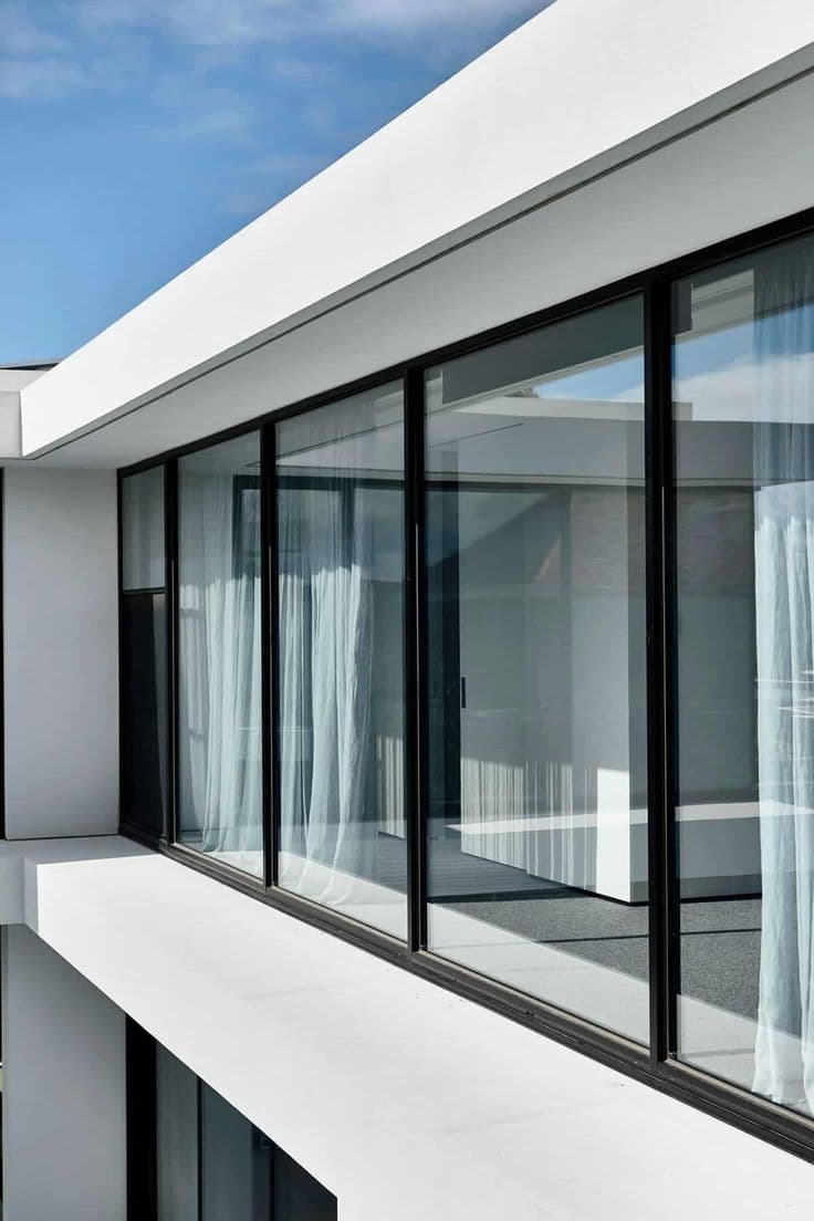 Fachada contemporânea com janelas de correr de alumínio preto do piso ao teto, vista em detalhe