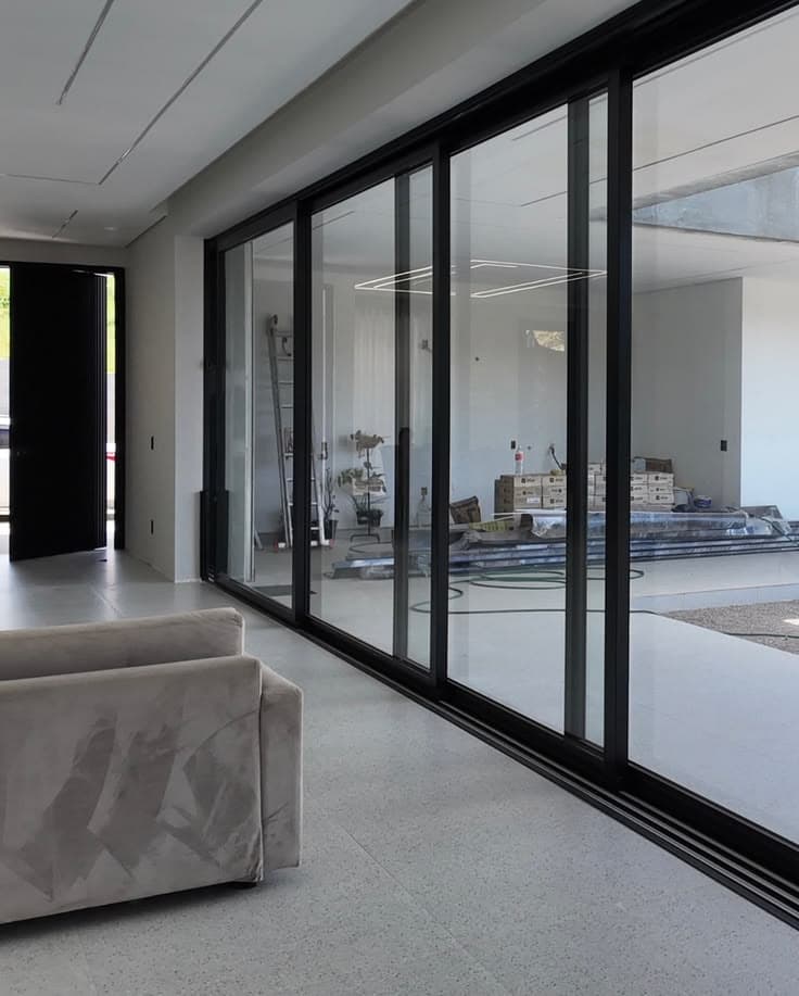 Porta de correr de alumínio preto em obra residencial, ambiente integrado com sala e terraço