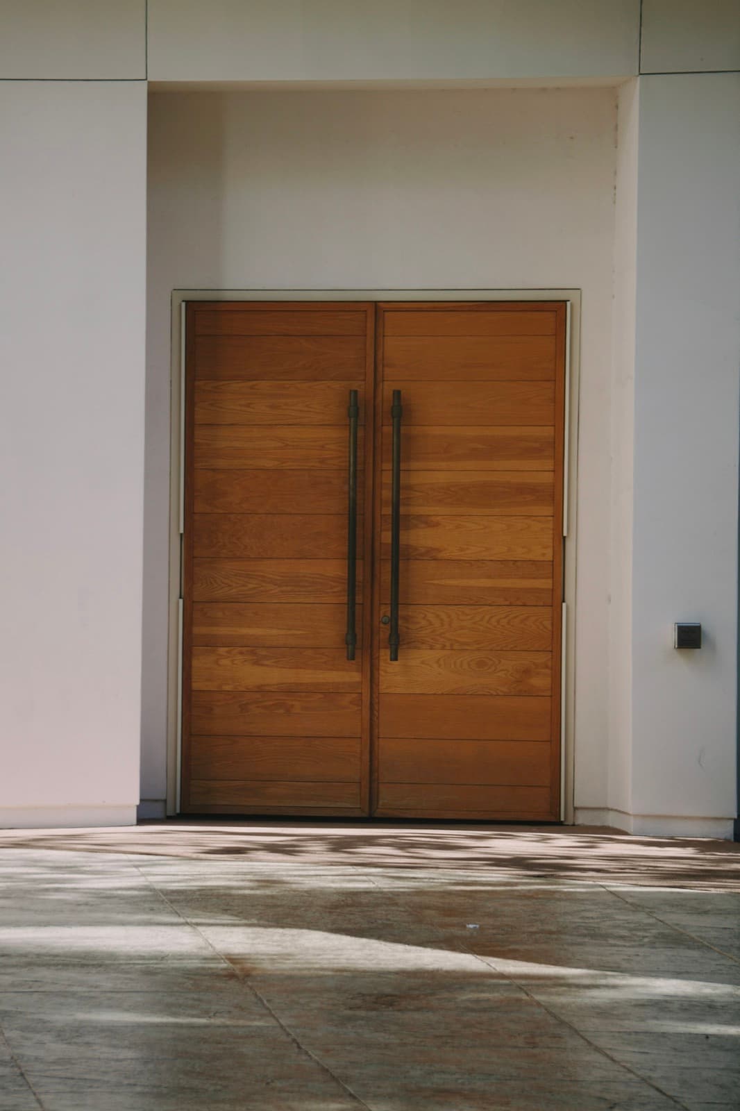 Porta dupla de madeira com puxadores pretos longos, em fachada branca minimalista (imagem de referência)
